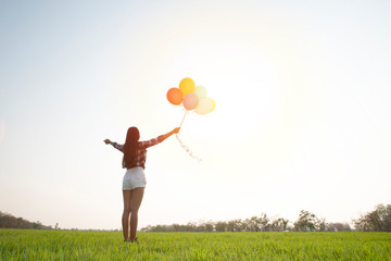 woman open arm with colorful balloon on the grass in the park