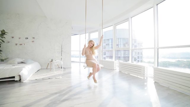 Beautiful woman swinging on a hanging swing in the bedroom. She smiles with happiness.