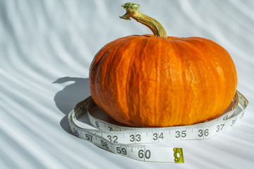 Fresh pumpkin with a measuring tape on a white background with bright light. The concept of diet...