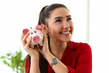 Portrait of young beautiful brunette woman holding pink piggy box for money