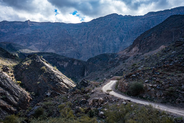 View of the dirt road between mountains on a cloudy day in Jebel Shams, Oman