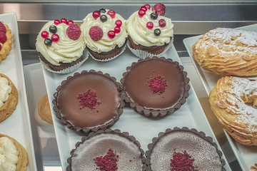 cakes with different fillings and colored glaze, decorated with fruits and berries behind the shop window, sweet dessert