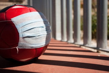 coronavirus concept in sport, soccer ball with breathing mask, closed soccer field fence