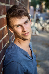 Delighted handsome man leaning against a brick wall giving a flirting look with a smile into the camera in an urban setting on a summer afternoon.