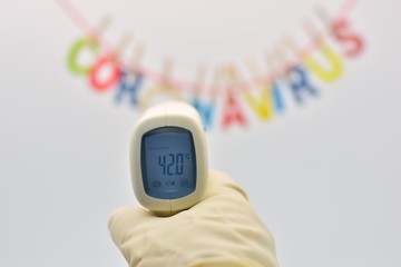 Termometro digital marcando 42 grados y la palabra coronavirus hecha con letras de colores...