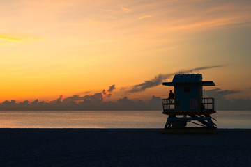 Guy enjoying the sunrise at Miami Beach from an iconic Miami Beach hut at the ocean during a calm summer morning (Florida, USA)