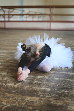 vertical photo of a little ballerina performing an exercise sitting on the floor