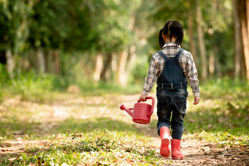 Back side of  asian little girl holding watering can walking  in to park