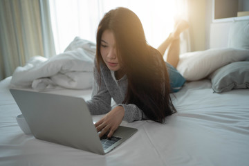 Fototapeta premium Attractive Young Asian Woman lying and using laptop computer on the bed in the morning.