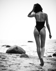 Beautiful lady in black swimsuit walks on a sandy beach