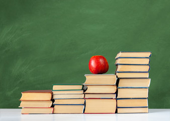 Back to school, pile of books and red apple with empty green school board background, education concept.