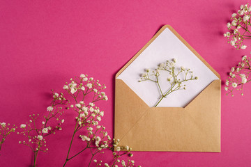 Kraft brown paper envelope with white empty card, gypsophila flowers, pink background, mockup blank letter