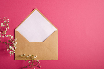 Kraft brown paper envelope with white empty card, gypsophila flowers, red pink background, mockup template