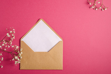 Kraft brown paper envelope with white empty card, gypsophila flowers, red pink background, mockup template