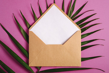 Kraft brown paper envelope with white empty card on palm leaves, pink purple background, mockup blank letter