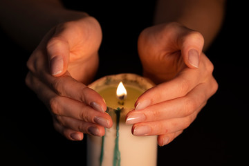 Women's hands above the burning candle close-up. Magic fire, the witch predicts. Isolate on a black background, a static shot