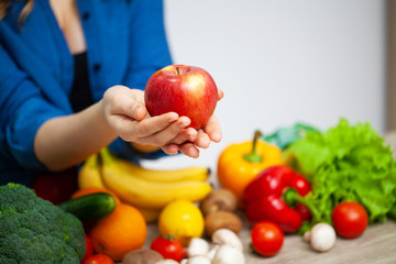 A woman at a table holding an apple on a background of fruit and vegetables