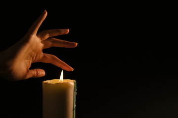 Esoterics and magic - women's hand conjure over a lit candle on a black background. Paronormal...