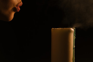 Spiritual session - a woman blows out a burning candle. Isolated, black background. The concept of religion, faith, magic and witchcraft