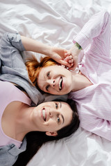 Obraz na płótnie Canvas Top view of same sex couple smiling while lying on bed