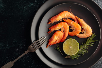 Boiled shrimps with rosemary and lime on a black plate.