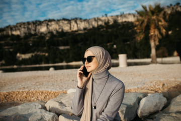 Beautiful portrait of young European Muslim women with hijab holding mobile phone and talking on the phone. She is happy and relaxed.