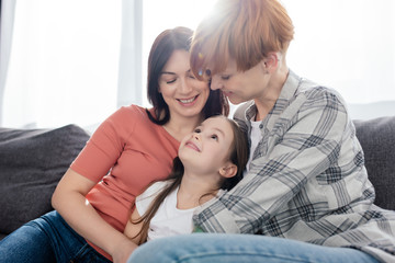 Same sex parents looking at smiling daughter on couch