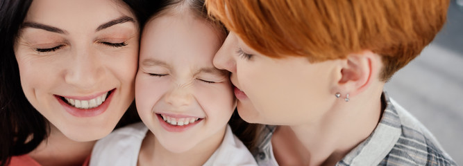 Panoramic shot of smiling same sex couple embracing daughter at home