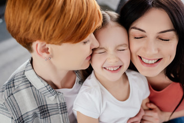 Obraz na płótnie Canvas Smiling same sex couple embracing kid at home