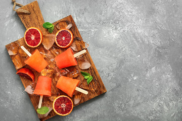 Frozen juice on a stick a red orange with mint leaves and ice on a wooden cutting board. Summer refreshing dessert. Popsicles. Top view, flat lay. © Yulia