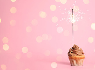 Birthday cupcake with sparkler on pink background. Space for text