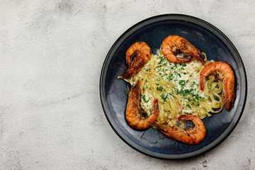 Fried prawns with tagliatelle in cream sauce in a plate on a light background. Top view, flat lay