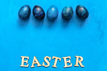 Easter eggs in turquoise blue on a blue painted background, border. Top view, flat lay.