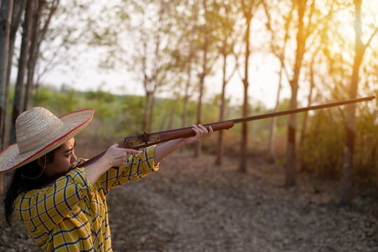 Portrait the farmer asea woman wearing a hat at the shooting range shot from a muzzle-loading vintage gun in the farm, Young girl standing in the attitude of aiming and looking through the sight rifle