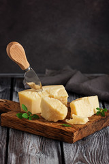 Parmesan cheese on a cutting board with basil leaves, rustic wooden table. Selective focus, dark background