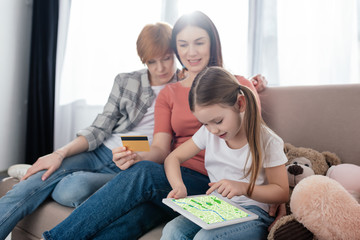 Child holding digital tablet with map app on screen near parents with credit card at home