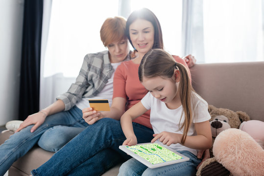 Child holding digital tablet with map app on screen near parents with credit card at home