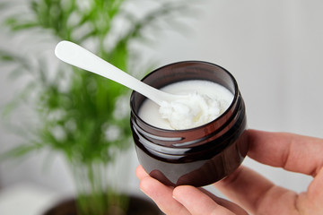 Shea butter in jar with spoon, cosmetic product for moisturizing skin. Female hand holds container...