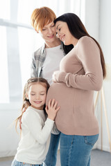 Smiling kid touching belly of pregnant mother near parent at home