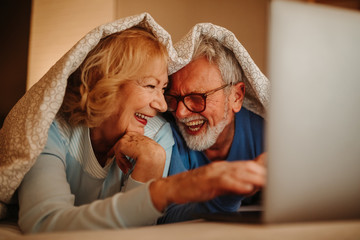 Love is everything! Smiling elderly couple lying in bed covered with blanket.