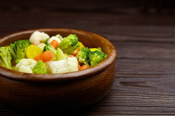Vegetable mix. Vegan food. Boiled broccoli, cauliflower and carrot in wooden bowl on wooden background. Healthy food. Steamed vegetables