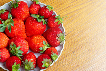 Fresh strawberries in white porcelain plate on wooden table