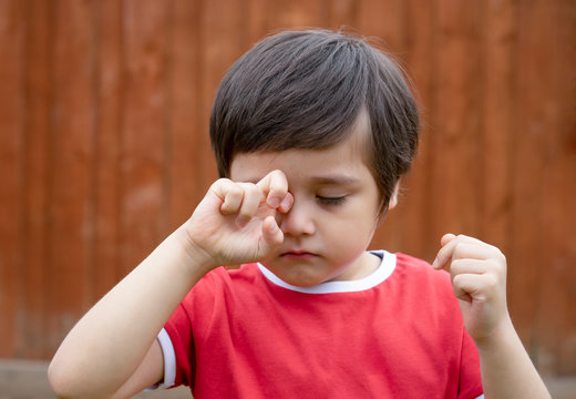 Little boy is having allergy rubbing his eye, Kid scratching his eyes while playing outdoor in summer, Child having allergy itchy face and sneezing while playing outdoor.