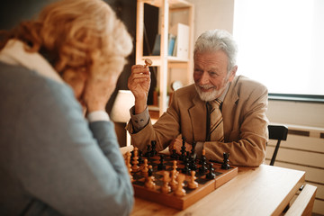 Portrait of happy senior man wearing suit and tie. He is winning in chess game against his wife.
