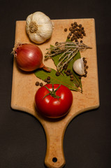 Brown cutting board for cooking with garlic tomatoes and  various spices top view