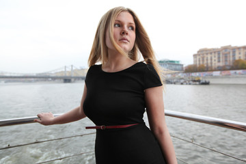Beautiful blonde in a black dress on a ship in the city