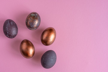 Colored painted pearl chicken eggs of violet, golden color on pink background. Minimalistic creative idea