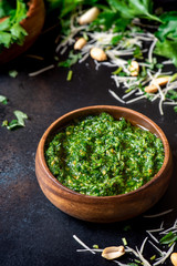 Homemade pesto sauce in a wooden bowl and ingredients for cooking on a black background close-up. Italian food.