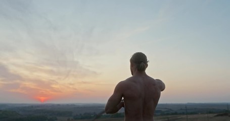 Confident strong man training with sword in nature during sunset