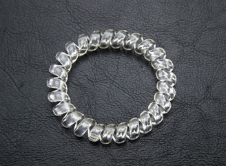 One transparent (colorless) spiral elastic for hair on a black leather, isolated background. A flexible plastic item for a female hairstyle or an arm bracelet. Elastic accessory